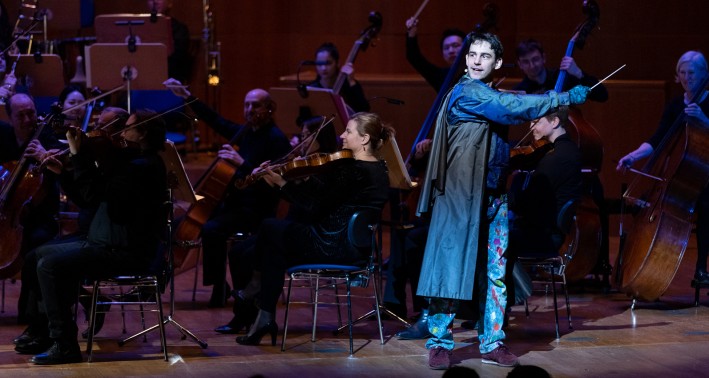 Schauspieler Jonathan Schimmer als Zauberlehrling auf der Bühne der Tonhalle, dahinter sitzt das Orchester