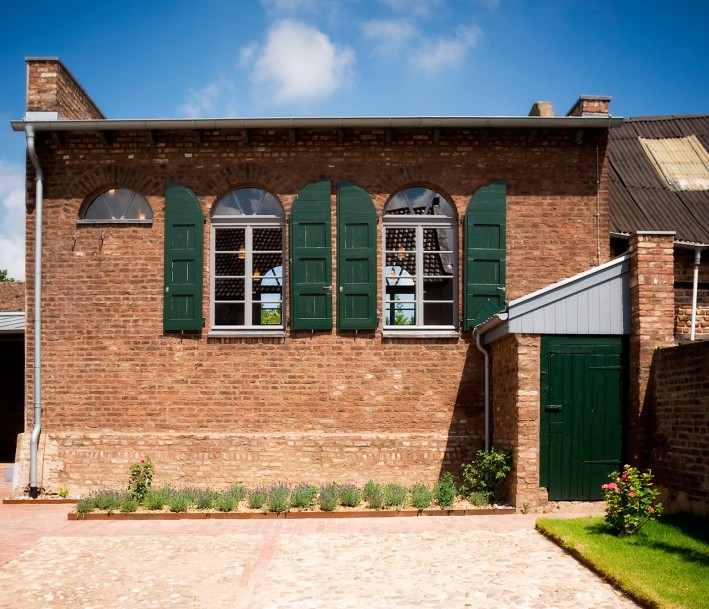 Ein Gebäude aus dem 19. Jahrhundert mit zwei großen Fenstern mit halbrunden Abschluss nach oben. Links befindet sich das kleine Halbrund-Fenster der Frauenempore.
