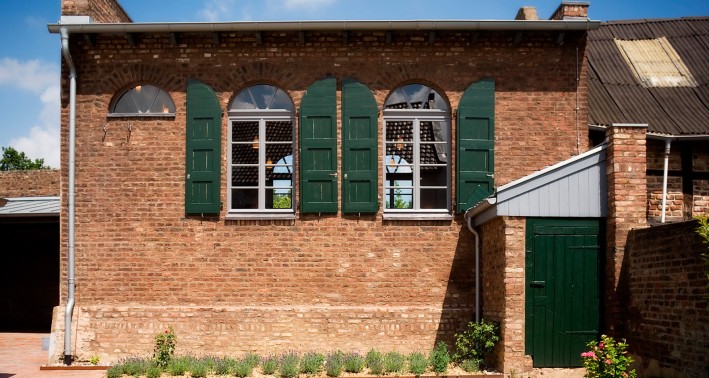 Ein Gebäude aus dem 19. Jahrhundert mit zwei großen Fenstern mit halbrunden Abschluss nach oben. Links befindet sich das kleine Halbrund-Fenster der Frauenempore.