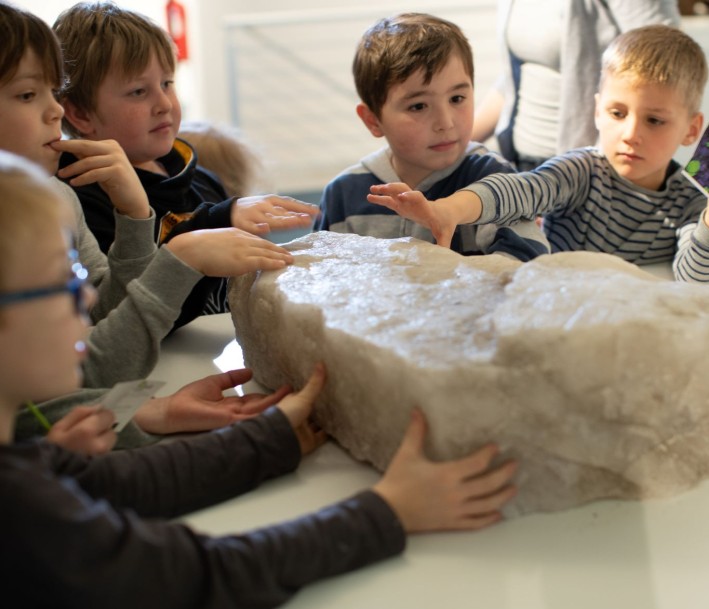 TuK Bad Sassendorf GmbH, Westfälische Salzwelten Das Bild zeigt eine Gruppe von Kindern, die einen großen Salzbrocken untersuchen und ertasten.