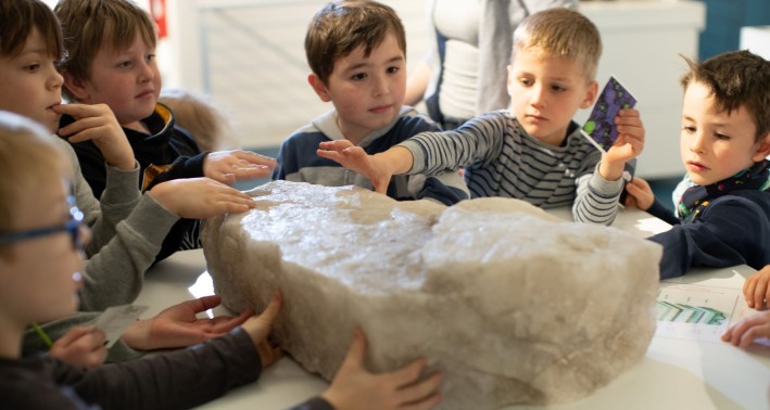 Das Bild zeigt eine Gruppe von Kindern, die einen großen Salzbrocken untersuchen und ertasten.