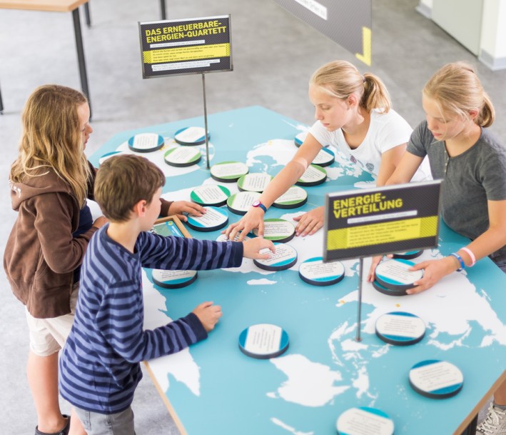 Kinder stehen an einem Tisch an dem eine Weltkarte abgebildet ist