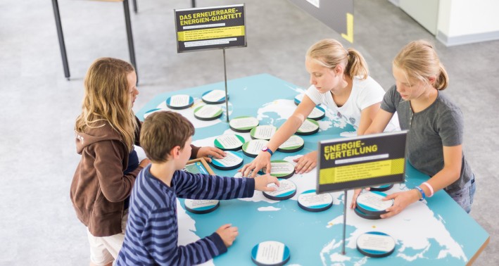Kinder stehen an einem Tisch an dem eine Weltkarte abgebildet ist