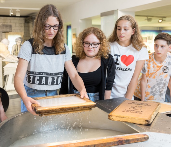 Fünf Schüler*innen an einer Papierbütte, die Papier schöpfen