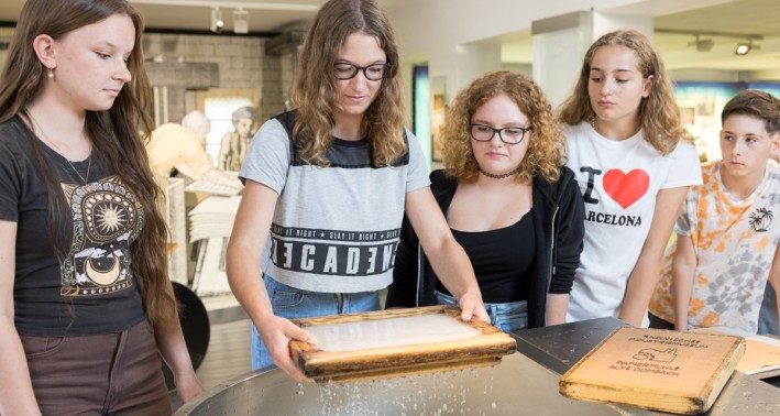 Fünf Schüler*innen an einer Papierbütte, die Papier schöpfen