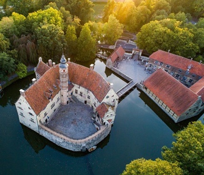 Foto: Tourismus NRW e. V. Das Bild zeigt eine Luftaufnahme der Burg Vischering, einer runden Ringmantelburg mit Burggraben ringsherum.