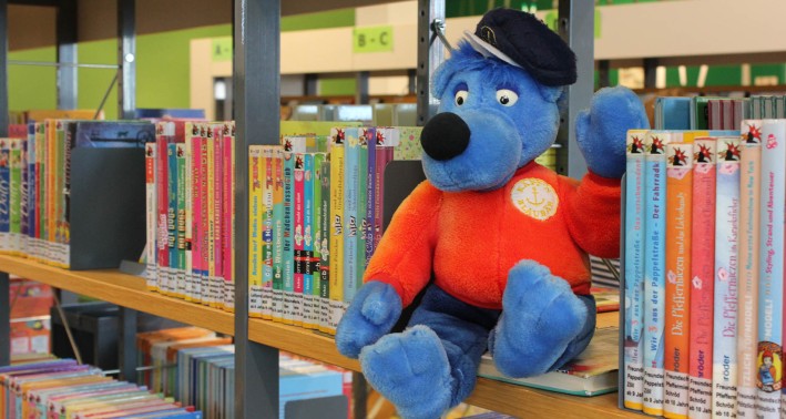 Das Bild zeigt ein Stofftier (von Käpt'n Blaubär) zwischen Kinderbüchern
