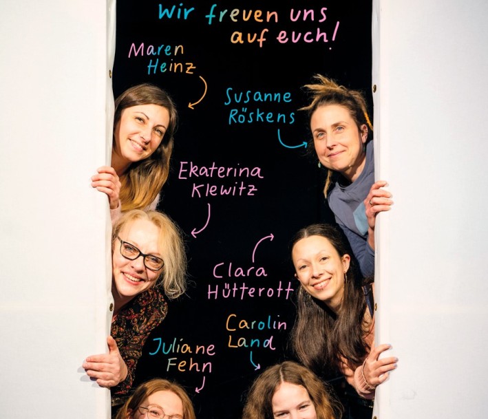 Auf dem Bild sind neun leute zu sehen, die aus einem Spalt gucken. Pfeile und bunte Buchstaben weisen ihnen jeweils einen Namen zu.