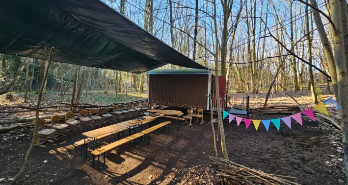 überdachte Sitzgruppe im Wald mit Bauwagen und bunten Wimpeln