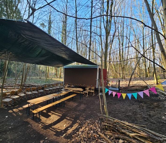 überdachte Sitzgruppe im Wald mit Bauwagen und bunten Wimpeln