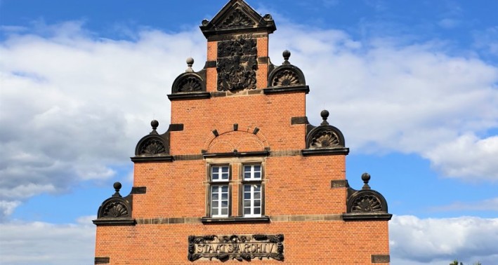 Das Bild zeigt ein rotes Backsteingebäude mit der Aufschrift 'Staatsarchiv'
