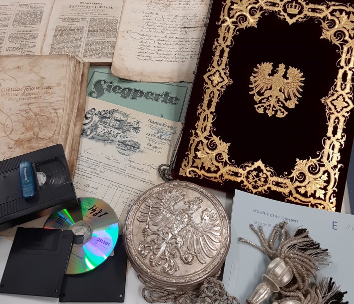 EIn Bild von verschiedenen Archivalien, darunter: CDs, Urkunden, Medaillon