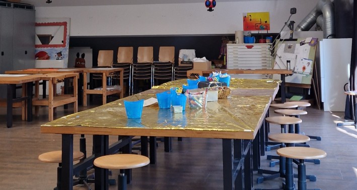 Blick in den Lernort. Es ist ein langer Arbeitstisch umrundet von Hockern zu sehen.