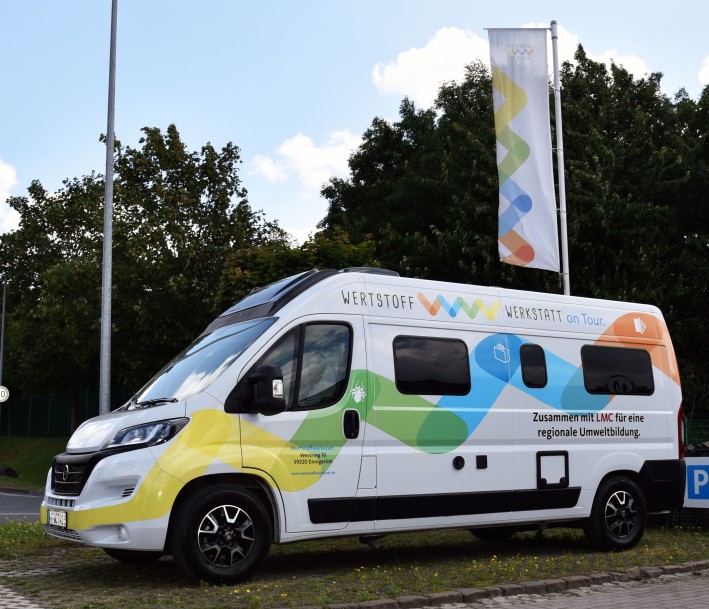 Foto: AWG Kreis Warendorf Umweltbildungsmobil am Standort Entsorgungszentrum in Ennigerloh. Das Auto ist in den selben bunten Farben gehalten und mit demselben Muster wie das Logo der Werkstoffwerkstatt.