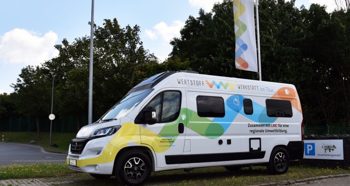 Umweltbildungsmobil am Standort Entsorgungszentrum in Ennigerloh. Das Auto ist in den selben bunten Farben gehalten und mit demselben Muster wie das Logo der Werkstoffwerkstatt.