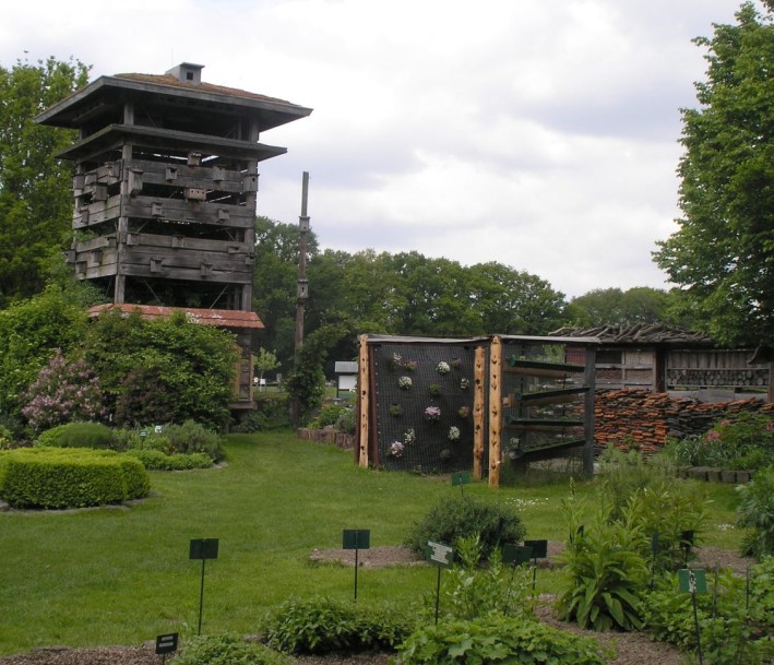 Blick auf das Gelände des Naturschutzhofs mit Beeten, Hecken und dem Lebensturm.