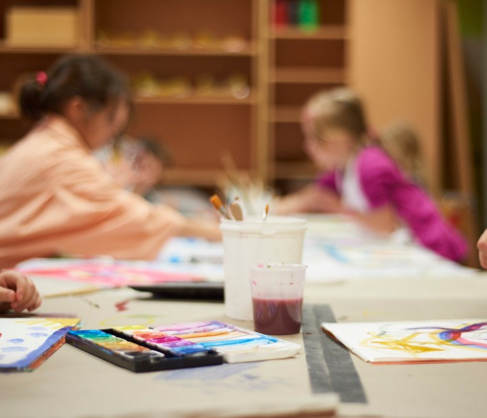 Tabea Borchardt Zu sehen sind enige Kinder, die gemeinsam an einem Tisch sitzen nd malen. Die Kinder sind nur verschwommen zu erkennen.