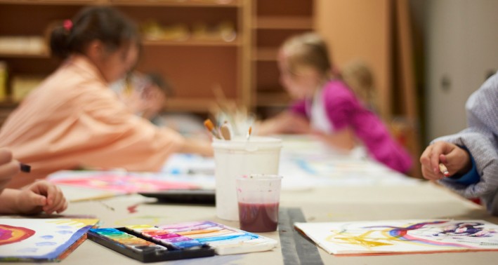 Zu sehen sind enige Kinder, die gemeinsam an einem Tisch sitzen nd malen. Die Kinder sind nur verschwommen zu erkennen.