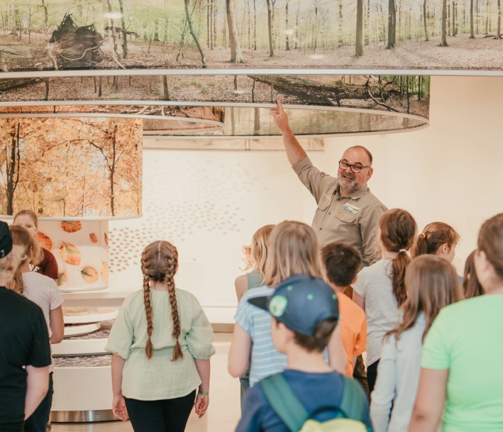 EIn Guide erklärt einer Gruppe von Schüler*innen etwas anhand eines Ausstellungsobjekts