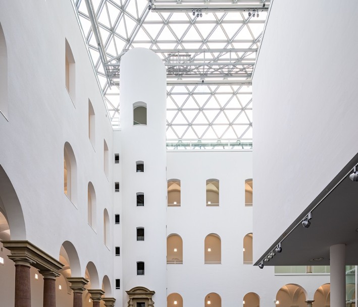 Foto: Kunstsammlung Nordrhein-Westfalen, Foto: Sebastian Drüen Eingangshalle mit Glasdecke und weißen Wänden mit Rundbogenfenster. Links befindet sich ein Säulengang.