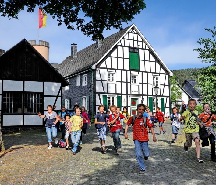 Foto: Maxx Hoenow Heimatmuseum in Bergneustadt. Eine Gruppe von Kindern läuft auf das Bild zu, im Hintergrund stehen ein paar Fachwerkhäuser.