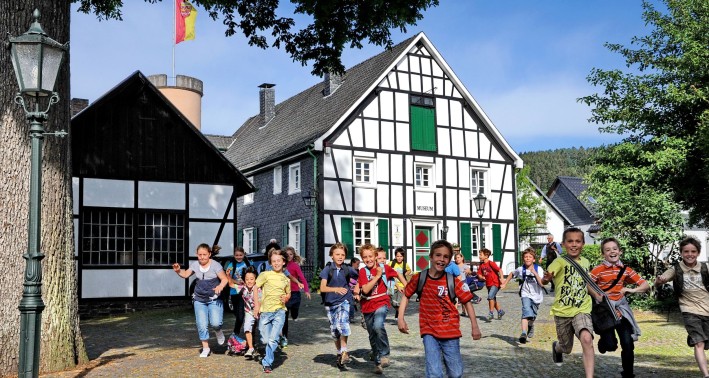 Heimatmuseum in Bergneustadt. Eine Gruppe von Kindern läuft auf das Bild zu, im Hintergrund stehen ein paar Fachwerkhäuser.