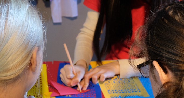 Impression Scherenschnitt: Das Bild zeigt eine Mitarbeiter*in, die zwei Schüler*innen anweist.