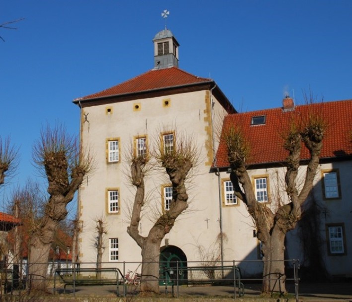 Foto: Biologiezentrum Bustedt Ostwestfalen-Lippe e.V. Fotografie eines Gebäudes mit heller Außenfassade und rötlichen Dach. Auf dem Dach befindet sich ein Dachreiter.