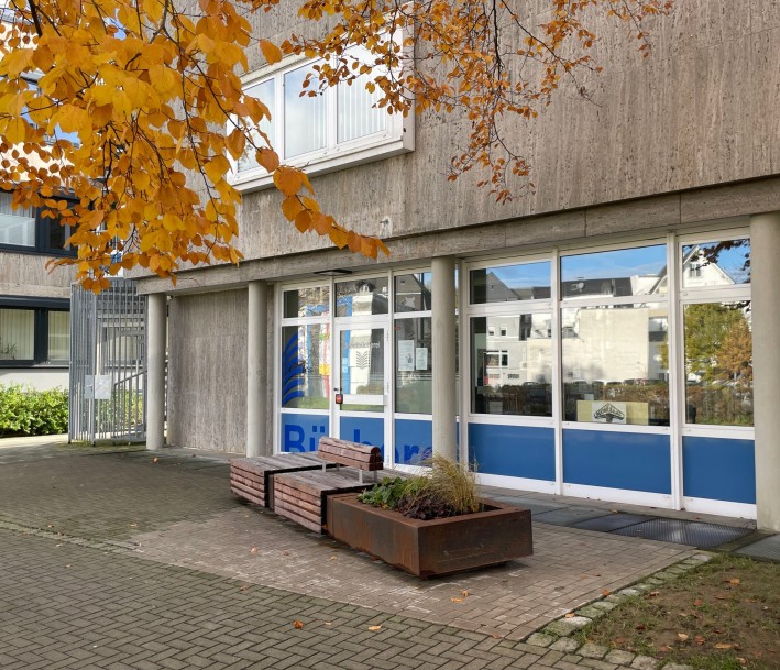 Foto: Stadtbücherei Meschede Außenfassade der Stadtbücherei Meschede. Vor dem Eingang befindet sich eine Bank und ein Pflanzkübel
