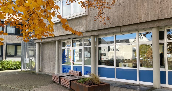 Außenfassade der Stadtbücherei Meschede. Vor dem Eingang befindet sich eine Bank und ein Pflanzkübel