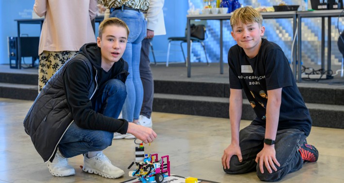 Das Bild zeigt zwei Schüler, die aus Bausteine Roboter bauen und diese jetzt auf einer Matte austesten