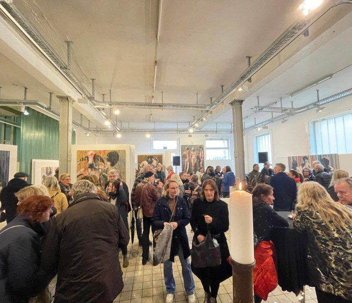 Foto: Raum für Kunst e. V. Ein weißer Veranstaltungsraum voller Leute. An den Seiten sind künstlerische Bilder zu sehen.