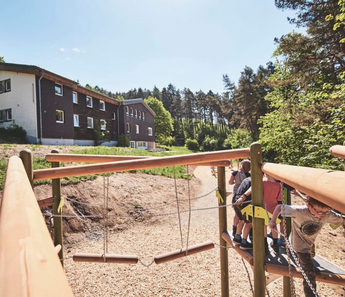 Außengeländer der Jugendherberge Rüthen mit dem Gebäude der Jugendherberge und Spielplatz mit Kindern. 