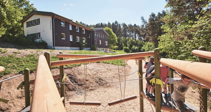 Außengeländer der Jugendherberge Rüthen mit dem Gebäude der Jugendherberge und Spielplatz mit Kindern.
