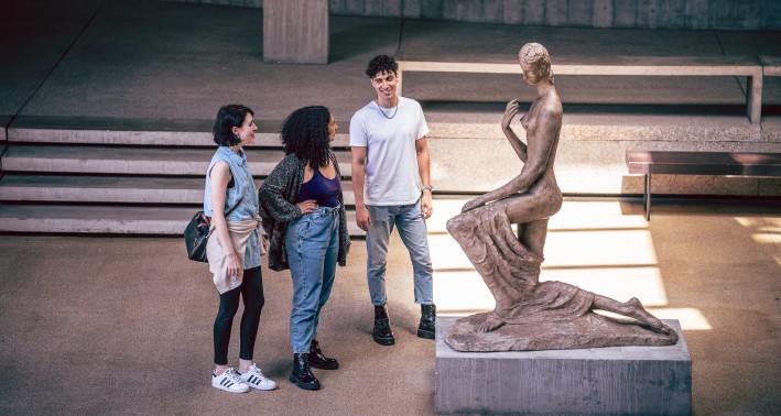 Eine Gruppe von drei Personen steht vor einer Plastik, die sich im Lehmbruck Museum befindet.
