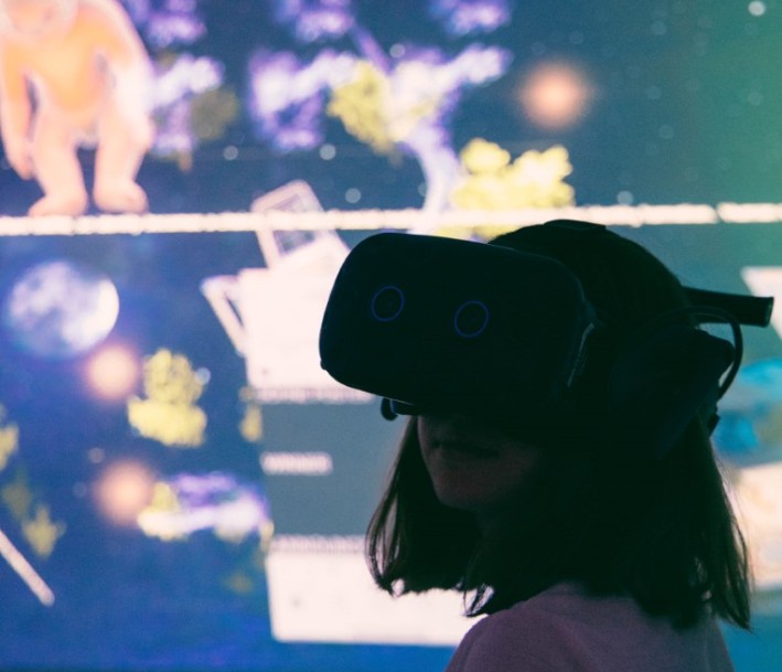 Person mit Virtual-Reality-Brille vor einer Wandprojektion mit verschiedenen abstrakten und figürlichen Elementen
