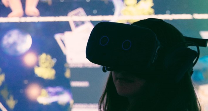 Person mit Virtual-Reality-Brille vor einer Wandprojektion mit verschiedenen abstrakten und figürlichen Elementen