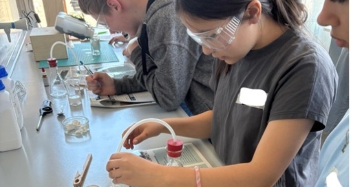 Mehrere Schüler*innen experimentieren mit Pipetten und Dokumentationsbögen. Sie tragen Schutzbrillen im Teutolab Biologie