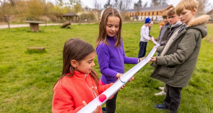 Pädagogisches Programm der help and hope Stiftung auf Gut Königsmühle. Mehrere Kinder halten eine selbst gebaute Kugelbahn auf einer grünen Wiese in den Händen.