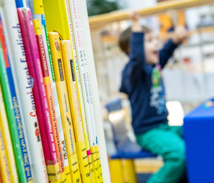 Eine Szene aus em Lernort Stadtteilbibliothek Erle: Bücher im Vordergrund, ein jubelndes Kind im Hintergrund