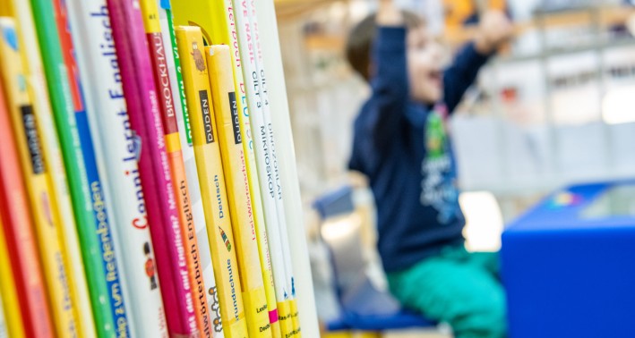 Eine Szene aus em Lernort Stadtteilbibliothek Erle: Bücher im Vordergrund, ein jubelndes Kind im Hintergrund