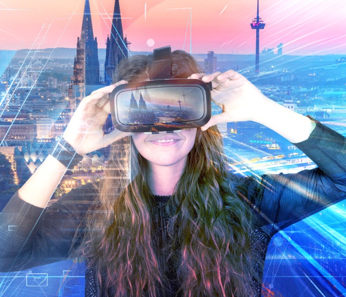Frau mit einer Virtual Reality Brille vor der Skyline Kölns