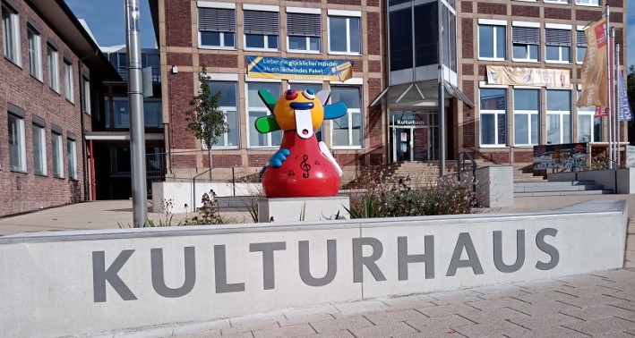 Das Foto zeigt eine Kunstfigur über dem Schriftzug 'Kulturhaus' auf einem Betonpodest.